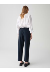 Marineblauwe stretchbroek met rechte snit, gecombineerd met een wit overhemd met lange mouwen, voorzien van een achterzak, platte schoenen en een gladde textuur.