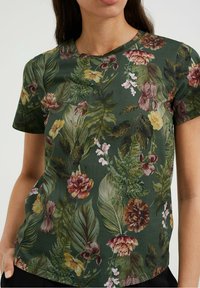 Květinové tričko v tmavě zelené barvě, s různými listy a květinami v barvách jako žlutá, růžová a kaštanově hnědá. Krátké rukávy, kulatý výstřih.