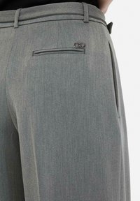 Light grey tailored trousers made of textured fabric, featuring a back pocket and a metallic logo accent.