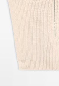 Light beige knitted sweater with a ribbed texture. Features a silver zipper detail at the neckline. Simple and minimalist design.