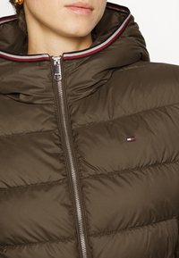 Giacca puffer marrone con cappuccio, dotata di zip argentata e dettagli a strisce rosse e bianche sul colletto. Design trapuntato compatto.