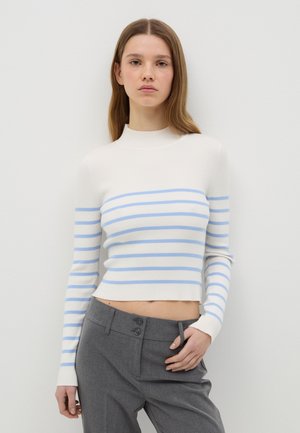 Pull en maille côtelée rayé blanc et bleu clair avec un col montant et un design cropped. Associé à un pantalon gris sur mesure avec deux boutons.