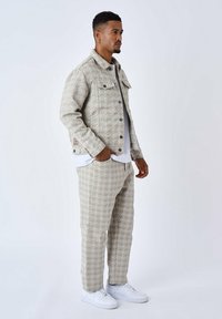 Chaqueta y pantalones de mezclilla beige con estampado y acentos blancos, con un diseño geométrico y botones en contraste, llevados con zapatillas blancas.