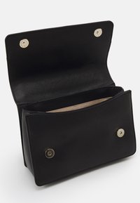 Sort læderhåndtaske med en tekstureret overflade, der har en tryklås og to åbne rum indeni. Indvendigt er den elfenbensfarvet.