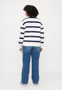 Hvit og marineblå stripet sweatshirt med avslappet passform, kombinert med lyseblå vide jeans og grå sneakers. Bakview synlig.