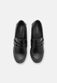 Pár černých kožených mokasín s prošívanými detaily a páskem přes přední část, zobrazeno z vrchu na bílém pozadí.