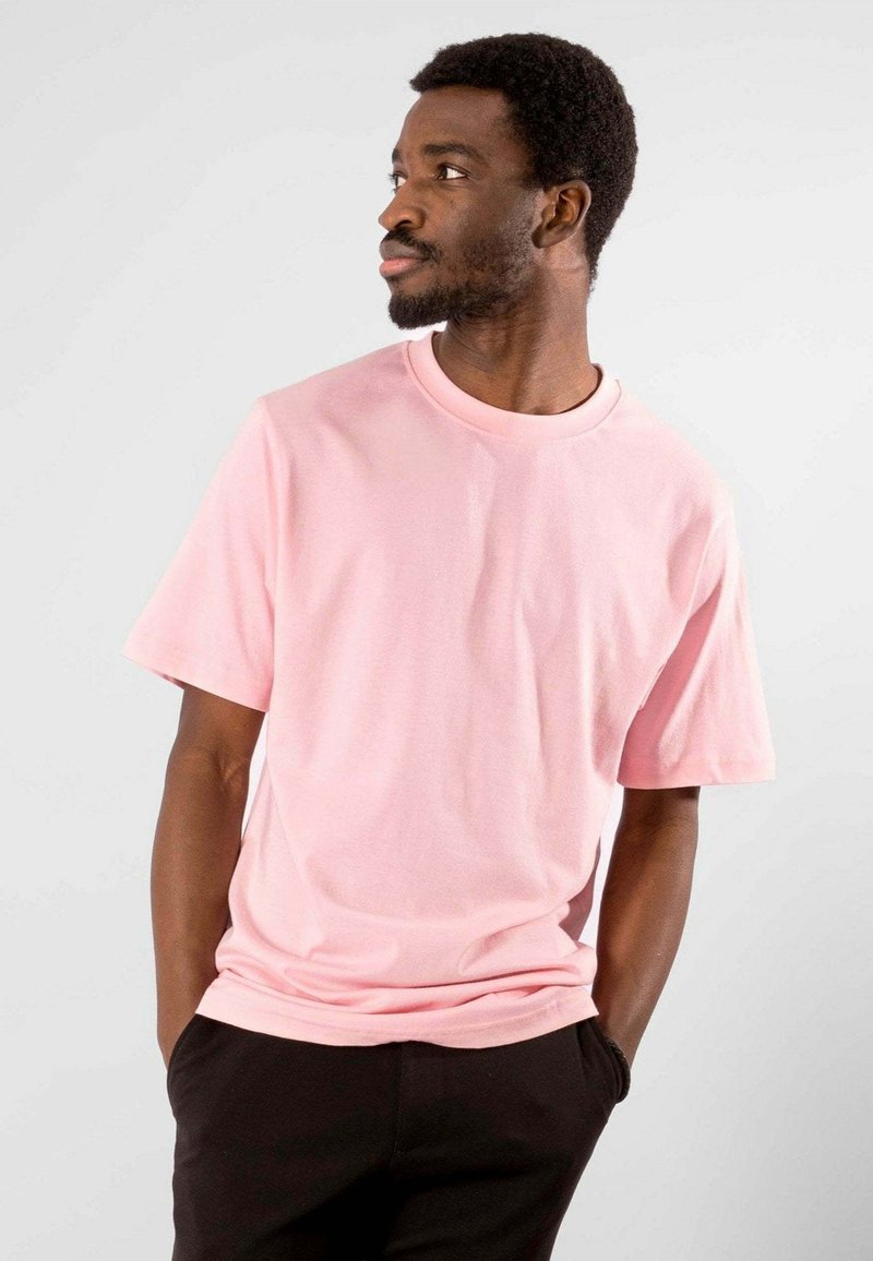Kortærmet t-shirt med rund hals i blødt pink stof; afslappet pasform med en glat tekstur, parret med sorte bukser. Enkelt design; ingen mønstre.