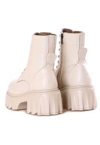 Botas de cuero beige hasta el tobillo con una suela de plataforma gruesa, cremallera lateral y adornos de botones decorativos a lo largo de la parte posterior.