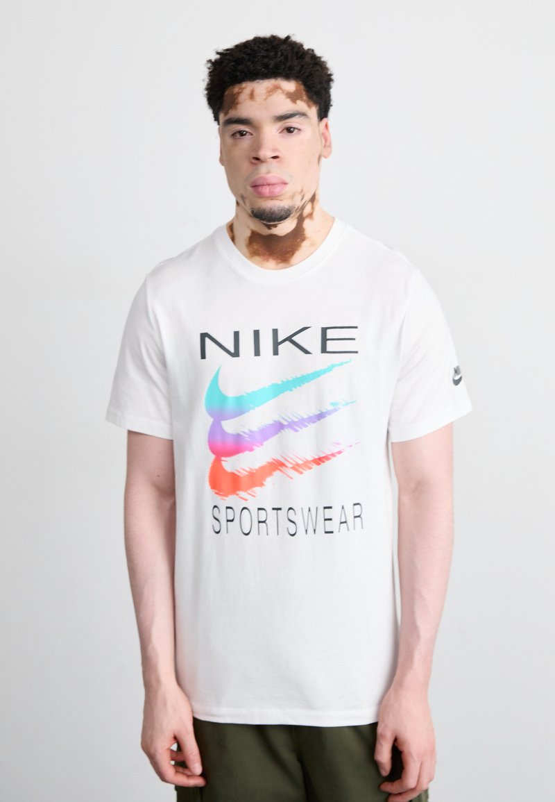 Balta medvilninė marškinėliai su spalvingu Nike logotipu, kuriame vyrauja mėlyni, rožiniai ir raudoni akcentai. Po logotipu bold stiliumi parašyta "SPORTO APRANGA".