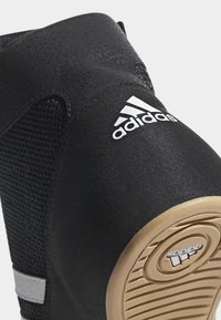 Black athletic shoe with mesh upper, rubber outsole, and white Adidas logo. Features a padded collar and grey accent strap.