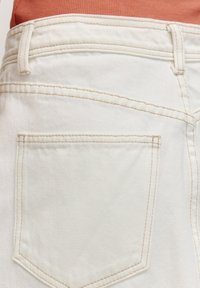 Jean en denim blanc avec une poche arrière, présentant des coutures beige contrastantes et une texture lisse. La ceinture est légèrement repliée.