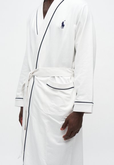 Peignoir blanc avec bordure noire, ceinture à la taille, poche avant et petit logo de joueur de polo sur la poitrine porté par une personne.