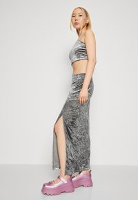 Metalický stříbrný dvoudílný outfit skládající se z kratšího topu a dlouhé sukně s bočním rozparkem. Doplněný lesklými růžovými platformovými botami.