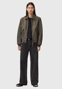 Καφέ δερμάτινο μπουφάν με φερμουάρ μπροστά, φαρδιά εφαρμογή, δύο μπροστινές τσέπες, μαύρο μπλουζάκι από κάτω, συνδυασμένο με μαύρο τζιν φαρδιάς γραμμής και μπότες.