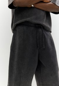 Pantaloni corti neri a vestibilità comoda realizzati in un tessuto morbido e testurizzato, con vita elasticizzata e cordoncino regolabile. Presentano tasche laterali e lunghezza al ginocchio.