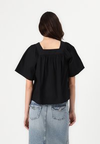 Top nero cropped con scollatura quadrata, maniche a sbuffo e dettagli arricciati sul retro. Abbinato a una gonna di jeans con tasche.