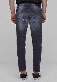Sötét mosású farmernadrág, Slim fit fazonnal, két hátsó zsebbel, finom kopással és kontrasztos varrással, fekete sportcipőkkel párosítva.