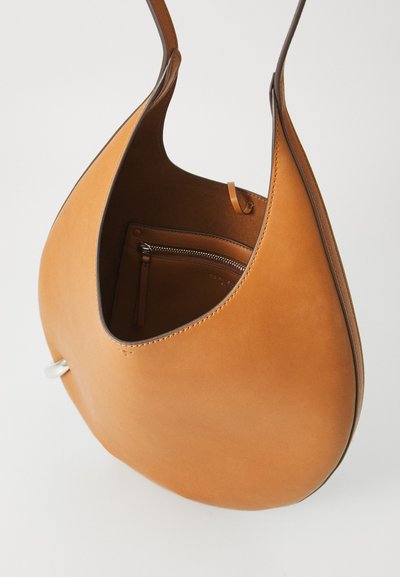 Brūns ādas plecu somiņa ar izliekta, asarveida formu. Iekšpusē ir rāvējslēdzēja kabata un tonāla šuvuma detaļas. Gluda tekstūra.