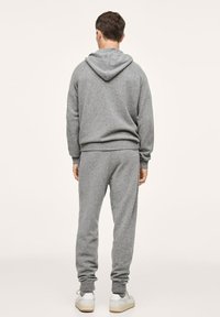 Grijze hoodie en bijpassende joggingsbroek van zacht stof, met ribgebreide manchetten en onderkant, een capuchon aan de achterkant en schoenen in een lichte kleur.