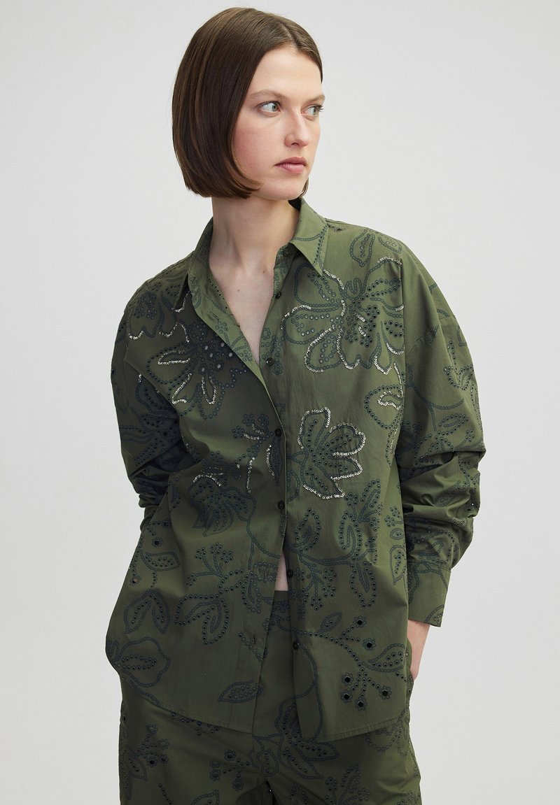 Olijfgroene button-up shirt met bloempatroon borduurwerk en zilveren draadaccenten. Beschikt over een klassieke kraag en losse mouwen.