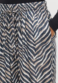 Calças com um tecido estampado em riscas zigzag em azul marinho, bege e branco, cintura elástica e bolsos laterais.