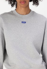 Gray sweatshirt made of soft fabric, featuring a ribbed crew neckline and a small blue "HUGO" label on the chest. Relaxed fit with long sleeves.