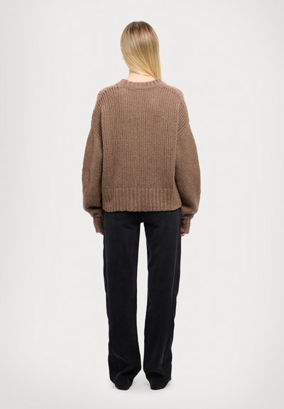 Suéter marrón de punto con un ajuste holgado, dobladillo acanalado y mangas anchas. Combinado con pantalones anchos negros, sin patrones ni acentos visibles.