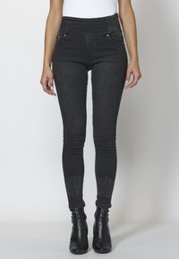 Svarta denim skinny jeans med hög midja, framfickor och nitar i nederkant. Texturerad tyg med en slät yta.