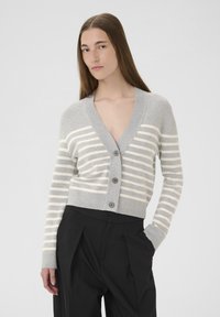 Sivý a krémový prúžkovaný cardigan s hlbokým V-výstrihom, zapínaním na gombíky a žebrovanými manžetami. Styling s čiernymi nohavicami s vysokým pásom.