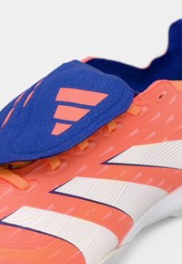 Zapatilla deportiva sintética de color naranja brillante con un talón y lengua azul, rayas blancas, parte superior texturizada y cordones naranjas en contraste.
