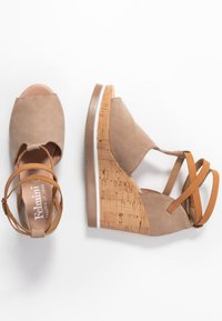 Sandales compensées beige avec talons en liège et bretelles en cuir marron clair autour de la cheville, design à bout ouvert, présentées sur un fond blanc.