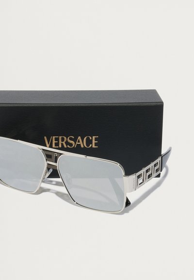 Srebrne prostokątne okulary przeciwsłoneczne z szarymi soczewkami, z dekoracyjną czarną wzorzystą zausznicą i wytłoczonym napisem "Versace" na czarnym etui.