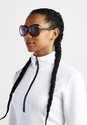 Lunettes de soleil avec une grande monture carrée, des verres foncés et un motif écaille de tortue. Portées avec un haut zippé blanc texturé arborant une garniture décorative.