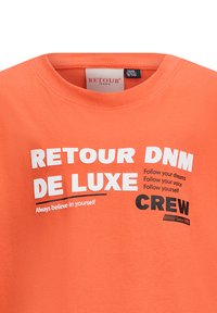 Pomarańczowa bawełniana koszulka z okrągłym dekoltem, z wyraźnym białym i czarnym tekstem, w tym brandingiem i motywacyjnymi hasłami, o gładkiej teksturze.