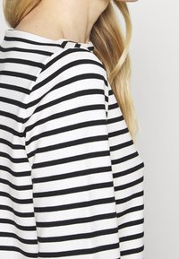 Black and white striped long-sleeve top with a round neckline, featuring a soft fabric and relaxed fit, visible from a side angle.