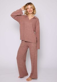Completo loungewear a coste di colore rosa tenue, con una maglietta a maniche lunghe con colletto e pantaloni a gamba larga, realizzati in tessuto testurizzato.