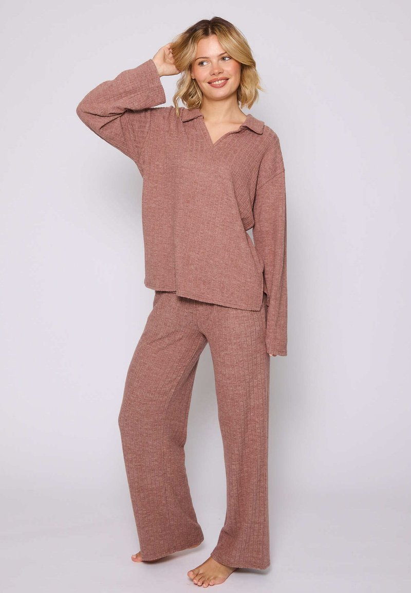 Completo loungewear a coste di colore rosa tenue, con una maglietta a maniche lunghe con colletto e pantaloni a gamba larga, realizzati in tessuto testurizzato.