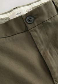 Pantalones rectos en verde oliva con una textura suave, cierre de botón y etiqueta en la cinturilla tejida. Presentan un brillo sutil y costuras finas.