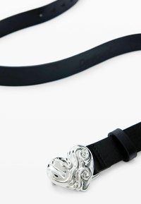 Cintura in pelle nera con fibbia a forma di cuore in argento caratterizzata da motivi intrecciati e superficie testurizzata.