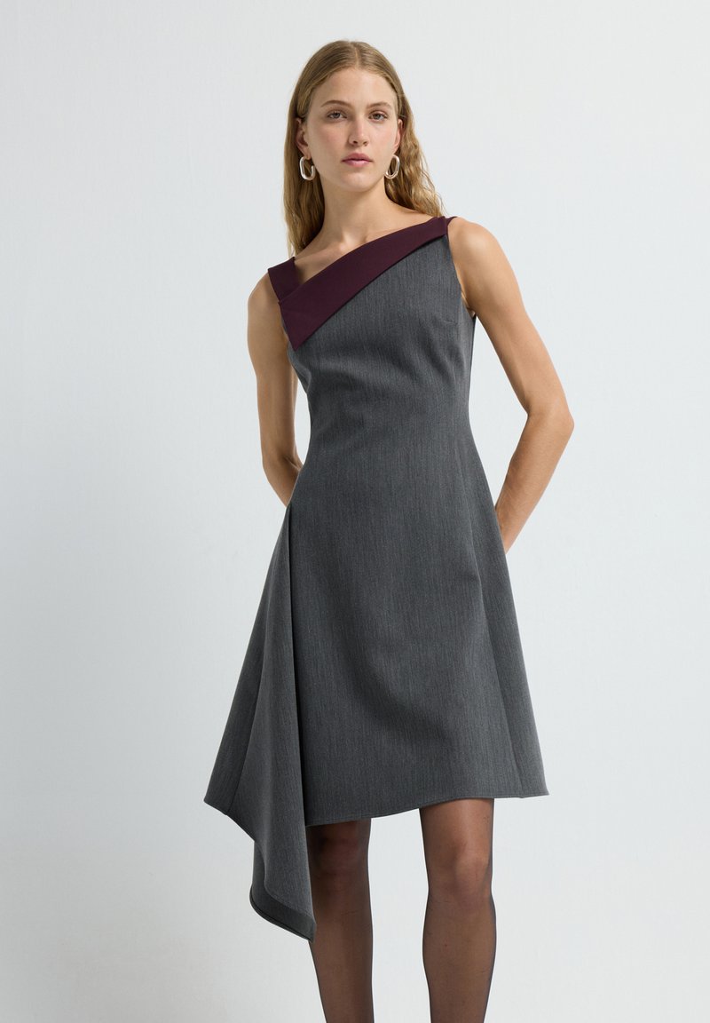 Graues Kleid mit strukturiertem Design, das einen diagonalen bordeauxroten Schulterriemen und einen asymmetrischen Saum aufweist.