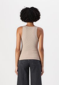 Lichtbruine geribbelde tanktop met een ronde hals en een aansluitend ontwerp. Gekleed met donkergrijze wijde broek, die een gladde textuur laat zien.