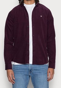 Camicia a maniche lunghe color bordeaux in tessuto corduroy, con colletto, chiusura a bottoni e piccolo logo sul petto.