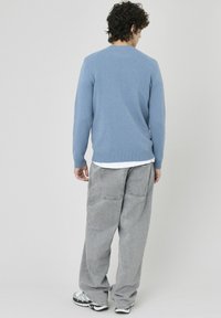Pull en maille bleu clair avec ourlet côtelé, associé à un pantalon gris ample. Vu de l'arrière, mettant l'accent sur le design et la texture.
