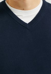 Pull col en V bleu marine en tissu doux avec bordure côtelée. Superposé à un t-shirt blanc à col rond, présentant une texture lisse et un design simple.