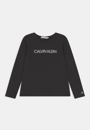 Sort langærmet skjorte med "CALVIN KLEIN" logo trykt i hvidt på brystet og lille "CK" logo nær venstre håndled.