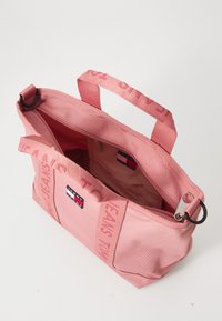 Roze canvas handtas met twee bovenhandvatten. Bevat een ritssluiting, interieurvoering en opvallende branding op de handvatten en de buitenkant.