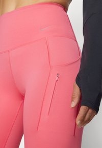 Leggings stretch roses avec une poche latérale zippée, une texture lisse et un détail logo discret près de la taille.