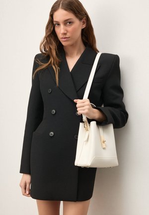Čierny dvojradový blejzer s vykrojenými klopami, textúrovanou tkaninou a dvoma prednými vreckami. Doplnok tvorí biela kabelka so zlatými detailmi.