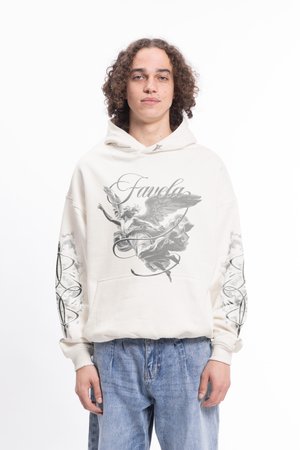 Krēmkrāsas krekls ar kapuci, uz kura ir grafiskais dizains, kas attēlo eņģeli un viļņveidīgas formas. Tam ir priekšējā kabata un ribotas aproces. Valkāts kopā ar zilām džinsām.