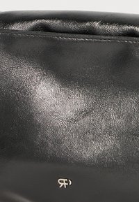 Borsa nera in finta pelle con una texture liscia e lucida. Presenta una leggera stampa del logo e un design minimalista.